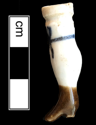 Porcelain leg, brown enamel boot and a blue bow made of Continental European hard paste porcelain. 3.75cm x 1cm - from 18MO609. Doll example on right from a private collection.